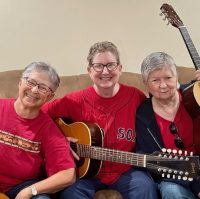 Three smiling musicians wearing red shirts